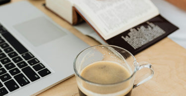 Woman Sitting at the Desk with a Laptop and a Cup of Coffee while Using a Paper Dictionary